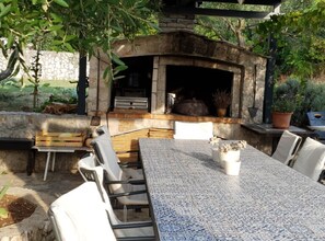 Une terrasse extérieure avec une cheminée en pierre, une table carrelée et des chaises.