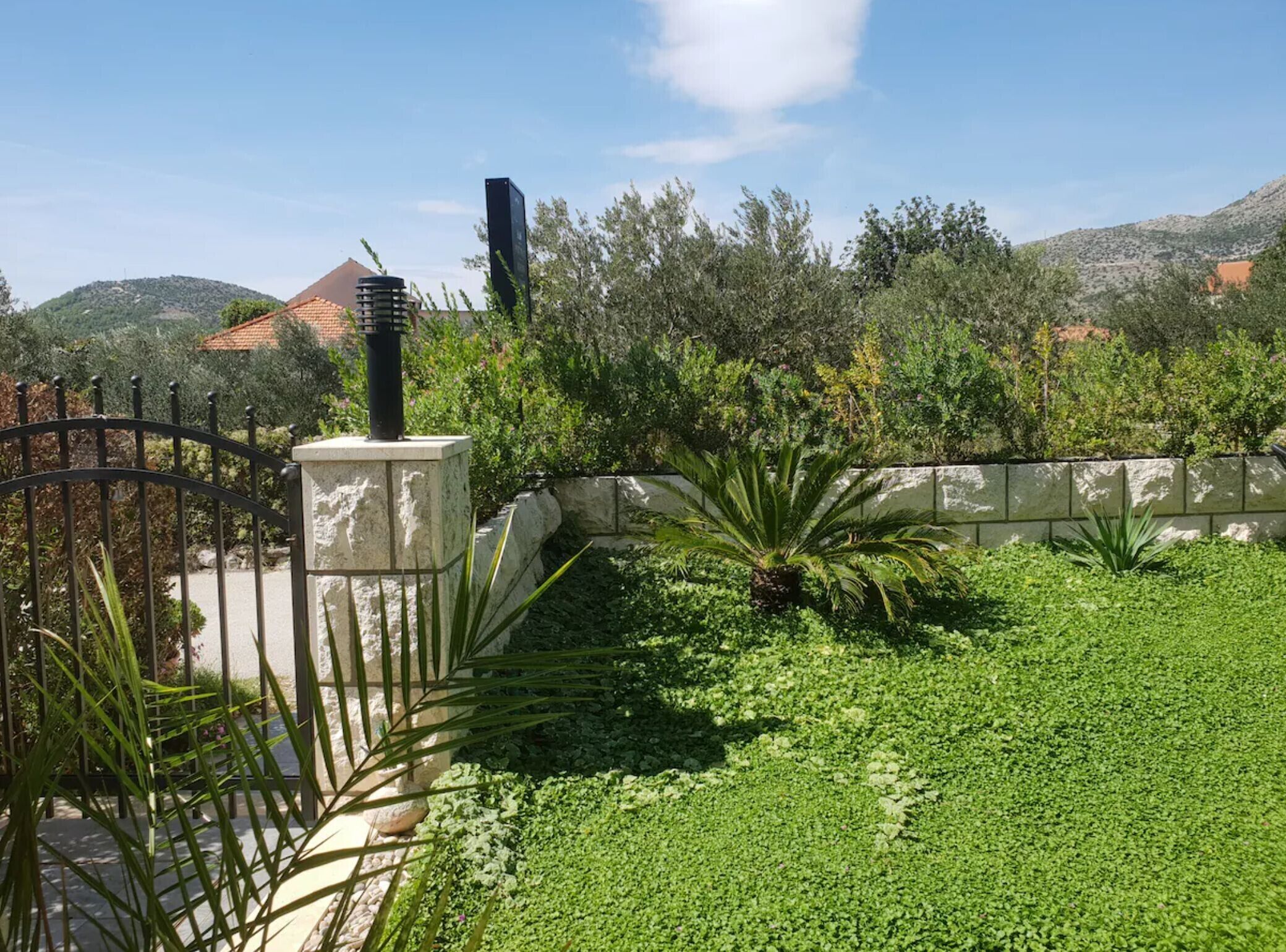 Un jardin aménagé avec un mur en pierre, une clôture en métal et une variété de plantes.