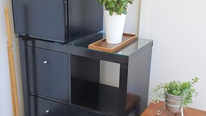 A black storage unit with drawers and a shelf, a wooden table with a potted plant, and a broom leaning against the wall. - Double Room with Terrace and Sea View (Slano)