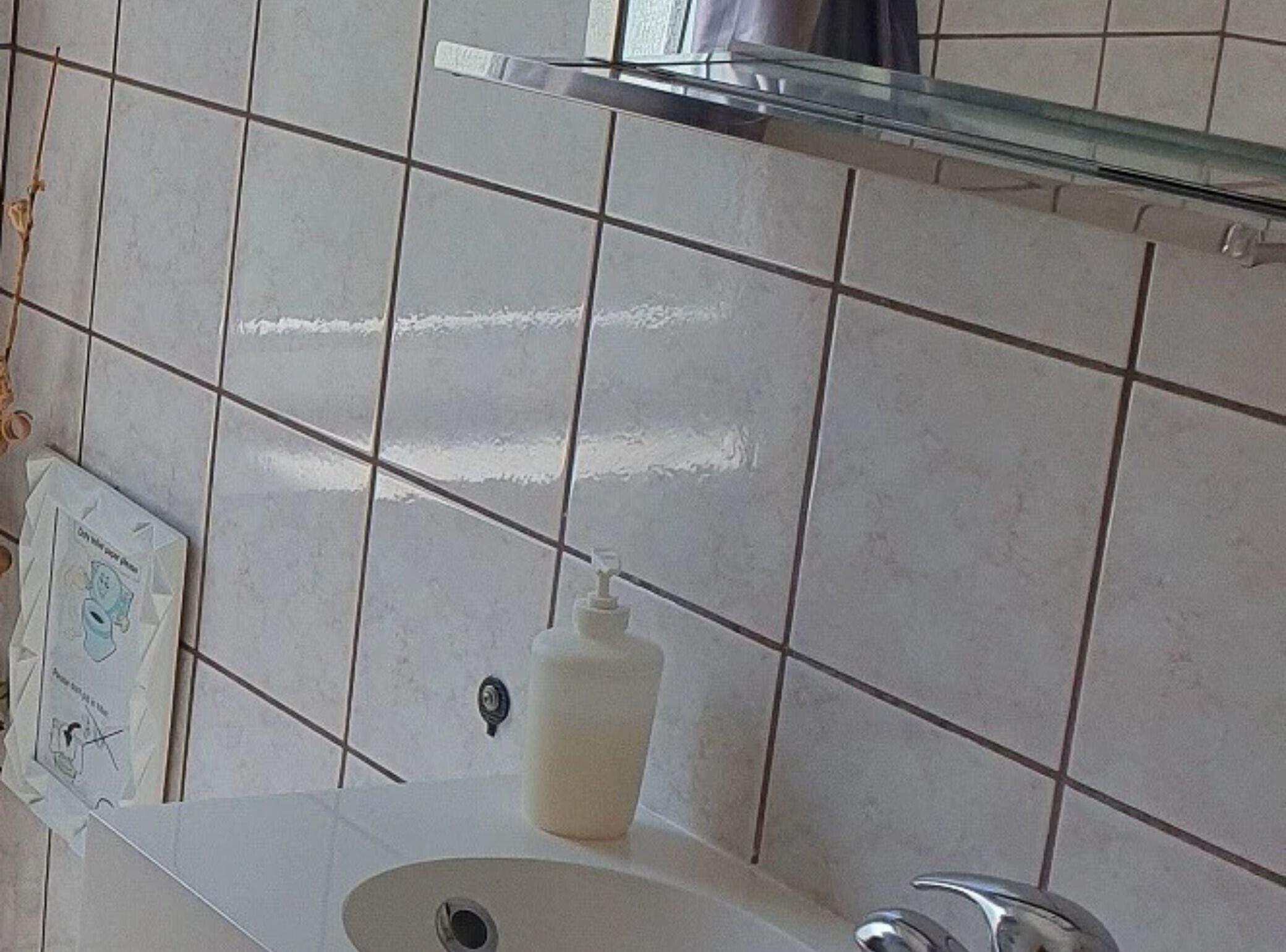 Un baño con un lavabo blanco, un espejo encima y un dispensador de jabón en la pared.