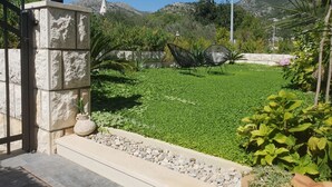 A well-maintained garden with a stone wall, a metal fence, and a clear view of a mountain in the background. - Double Room with Terrace and Sea View (Slano)