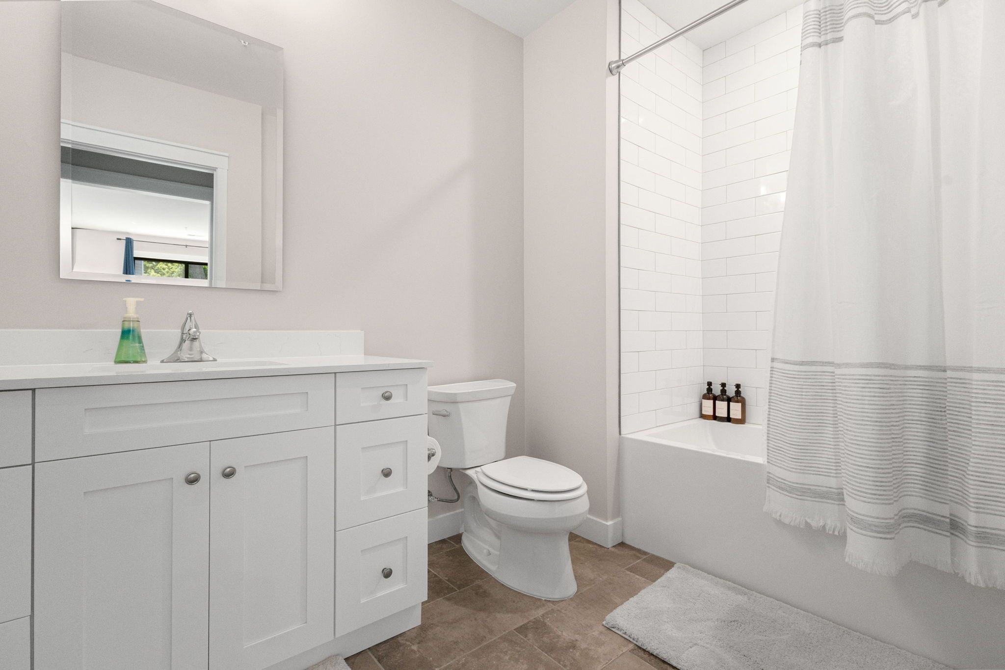 A modern bathroom with a white vanity, a toilet, a shower with a curtain, and a mirror above the vanity.