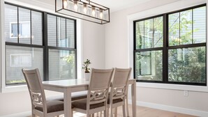 A dining area with a table and chairs, large windows, and a hanging light fixture. - Luxury Modern Condo Near Notre Dame 2BD| 2BA (South Bend)