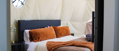 A bedroom with a bed, pillows, a bedside table, a lamp, and a rug.