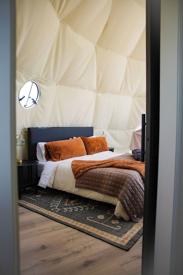 A bedroom with a bed, pillows, a bedside table, a lamp, and a rug.