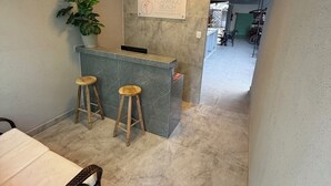 Quarto de hotel com cama, pequeno bar com banquetes, planta em vaso e um aviso na parede.