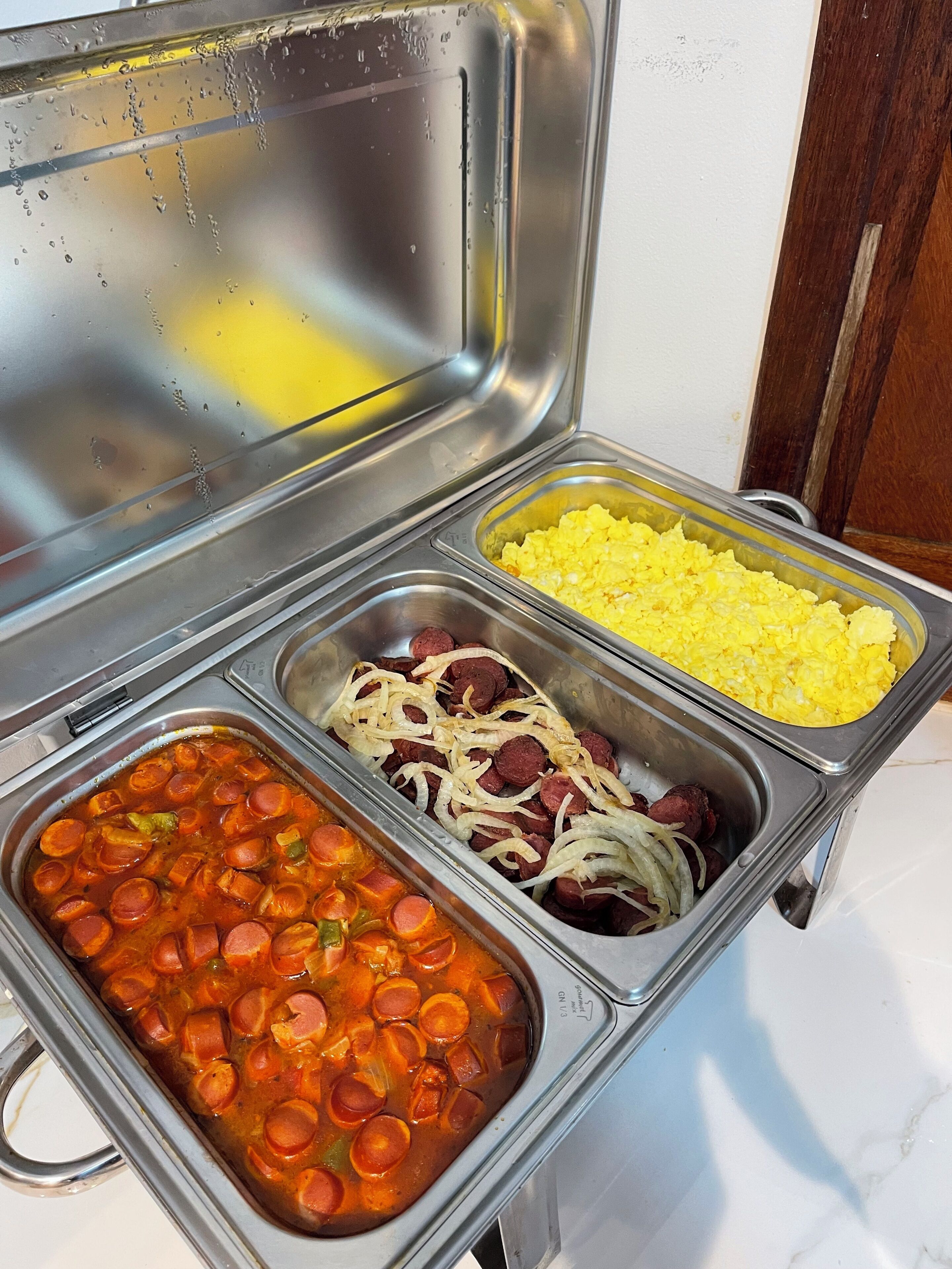 A buffet with various food options including scrambled eggs, sausage with onions, and a chili-like dish.