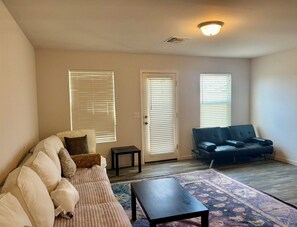 A living room with a sofa, a coffee table, and a patterned rug. There are two doors with blinds and a ceiling light fixture. - Awesome 3-bedroom house with AC in pleasant Kingman (Kingman)