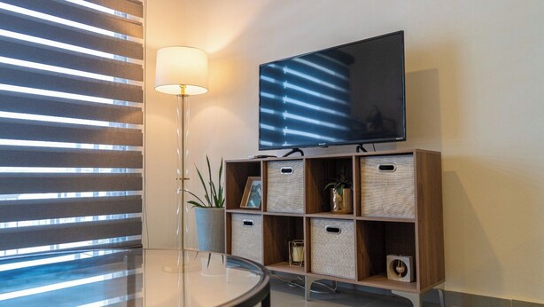 A modern room with a flat-screen TV mounted on a wooden shelf, a glass table, and a floor lamp.