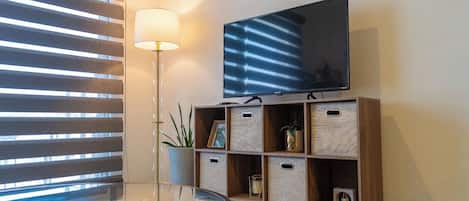 A modern room with a flat-screen TV mounted on a wooden shelf, a glass table, and a floor lamp.