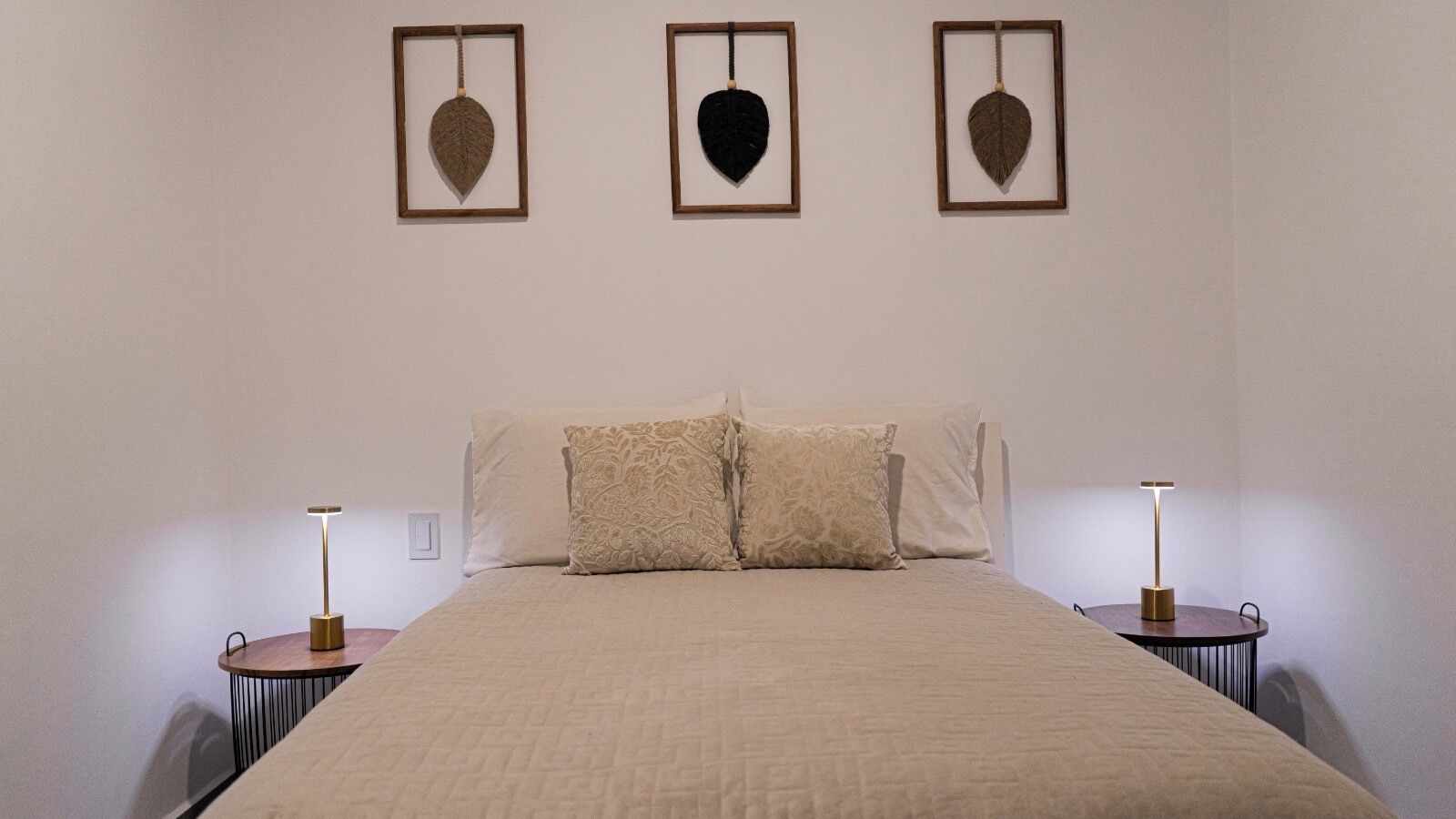 Ein Schlafzimmer mit einem Bett, zwei Nachttischen und drei gerahmten Blättern an der Wand.