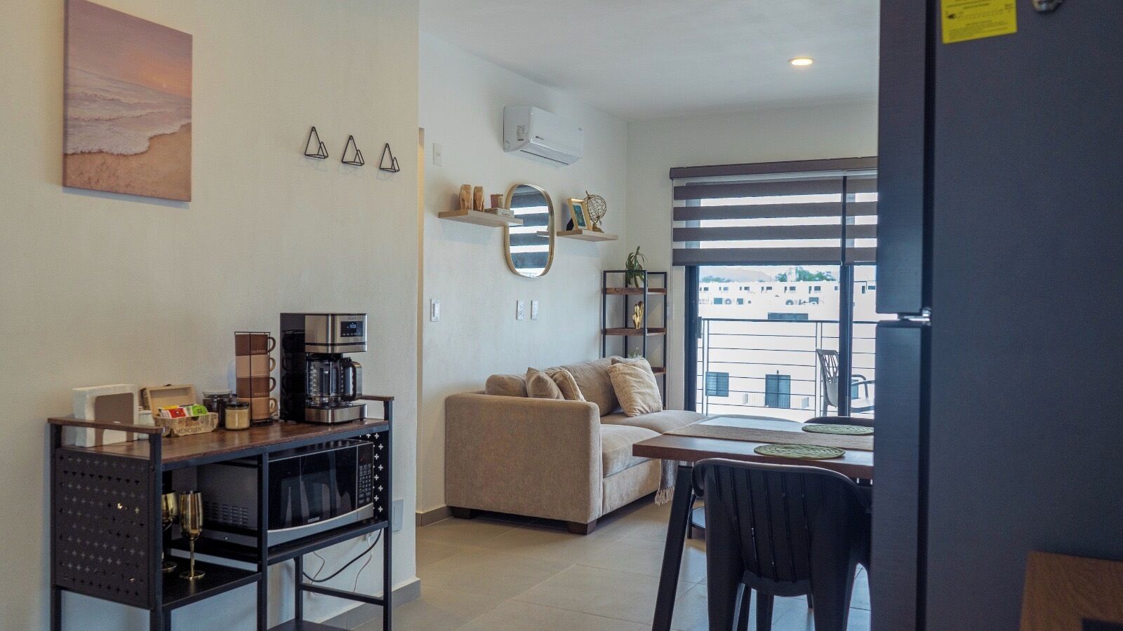 A modern living room with a sofa, a coffee station, and a dining area with a table and chairs.