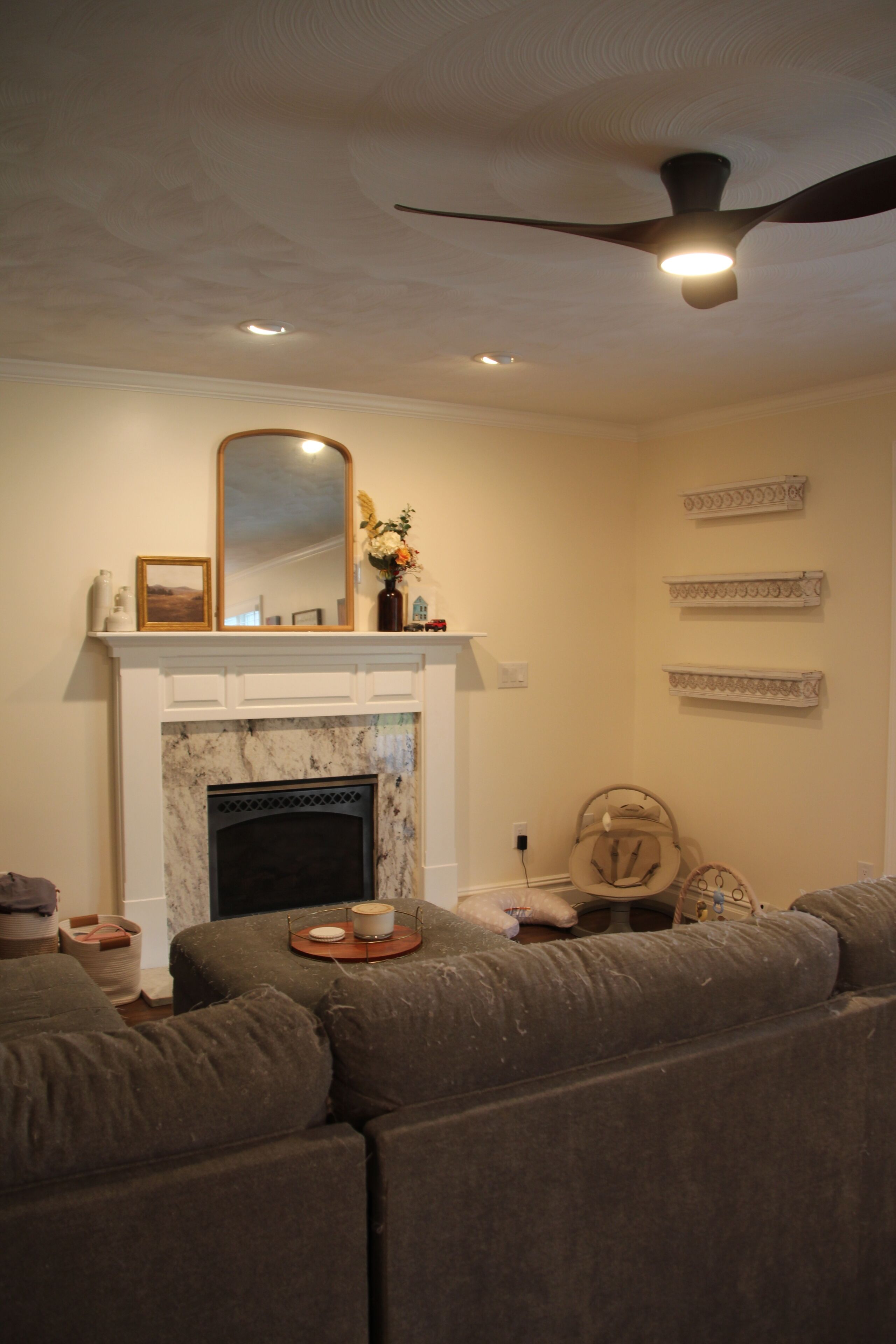 A living room with a fireplace, a ceiling fan, and a large sectional sofa.