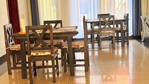 Un comedor con mesas y sillas de madera, una vela sobre una mesa, y vistas a través de cortinas traslúcidas.
