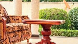 Una mesa de madera con base tallada, un sofá estampado y un jardín bien cuidado al fondo.