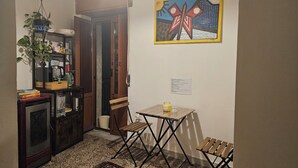 Un espace de vie compact comprenant un coin cuisine, un coin repas avec une petite table et des chaises, une plante en pot et un tableau accroché au mur.