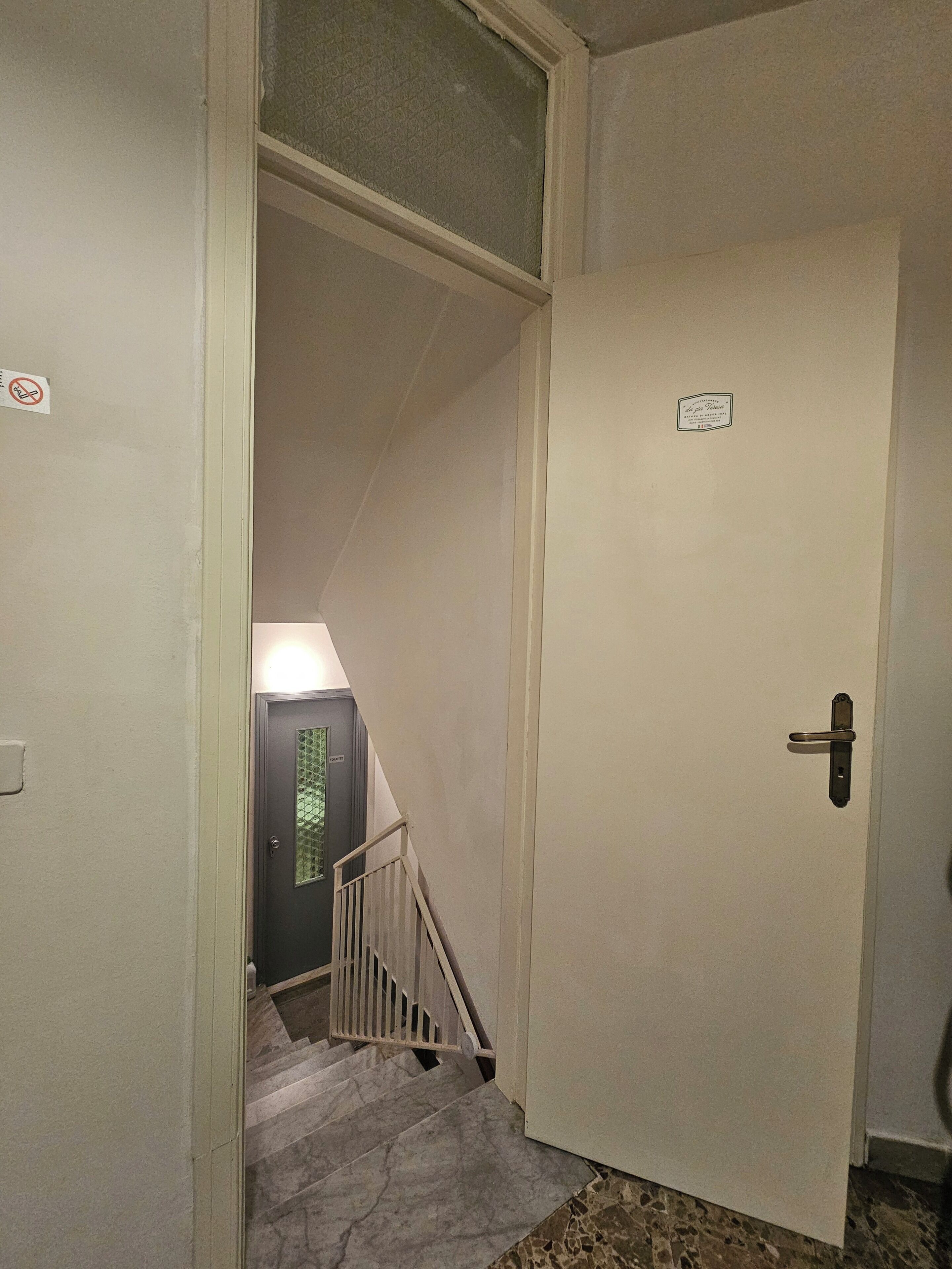 Un couloir avec une porte, un escalier et un luminaire fixé au mur.