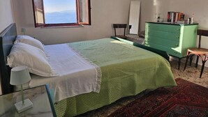 Une chambre à coucher avec un lit, une commode verte, une chaise, un bureau, une fenêtre et un tableau accroché au mur.