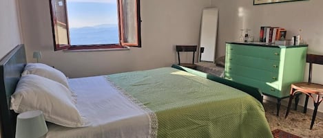 A bedroom with a bed, a green dresser, a chair, a desk, a window, and a painting on the wall.