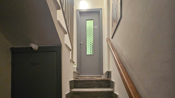 Un escalier menant à une porte sur laquelle figure un symbole de toilettes, une autre porte avec l’inscription « Interdit de fumer » et une main courante sur la droite.