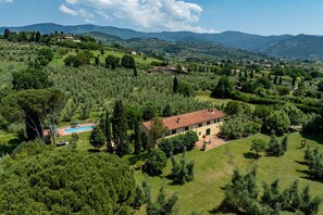 Eine Villa mit Swimmingpool, umgeben von üppiger Vegetation und Bergen im Hintergrund.