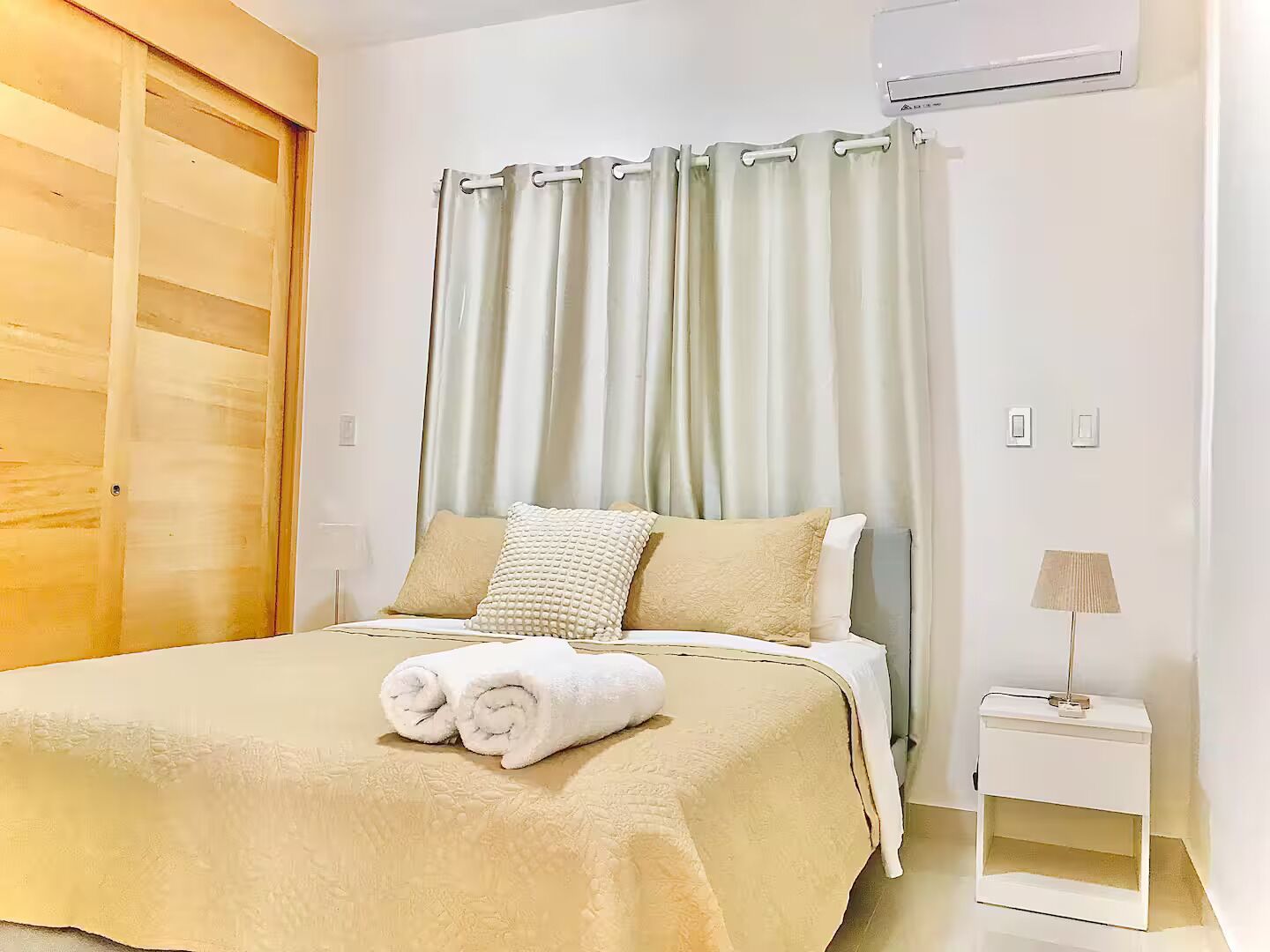 A bedroom with a bed, a nightstand, a lamp, and a window with curtains.