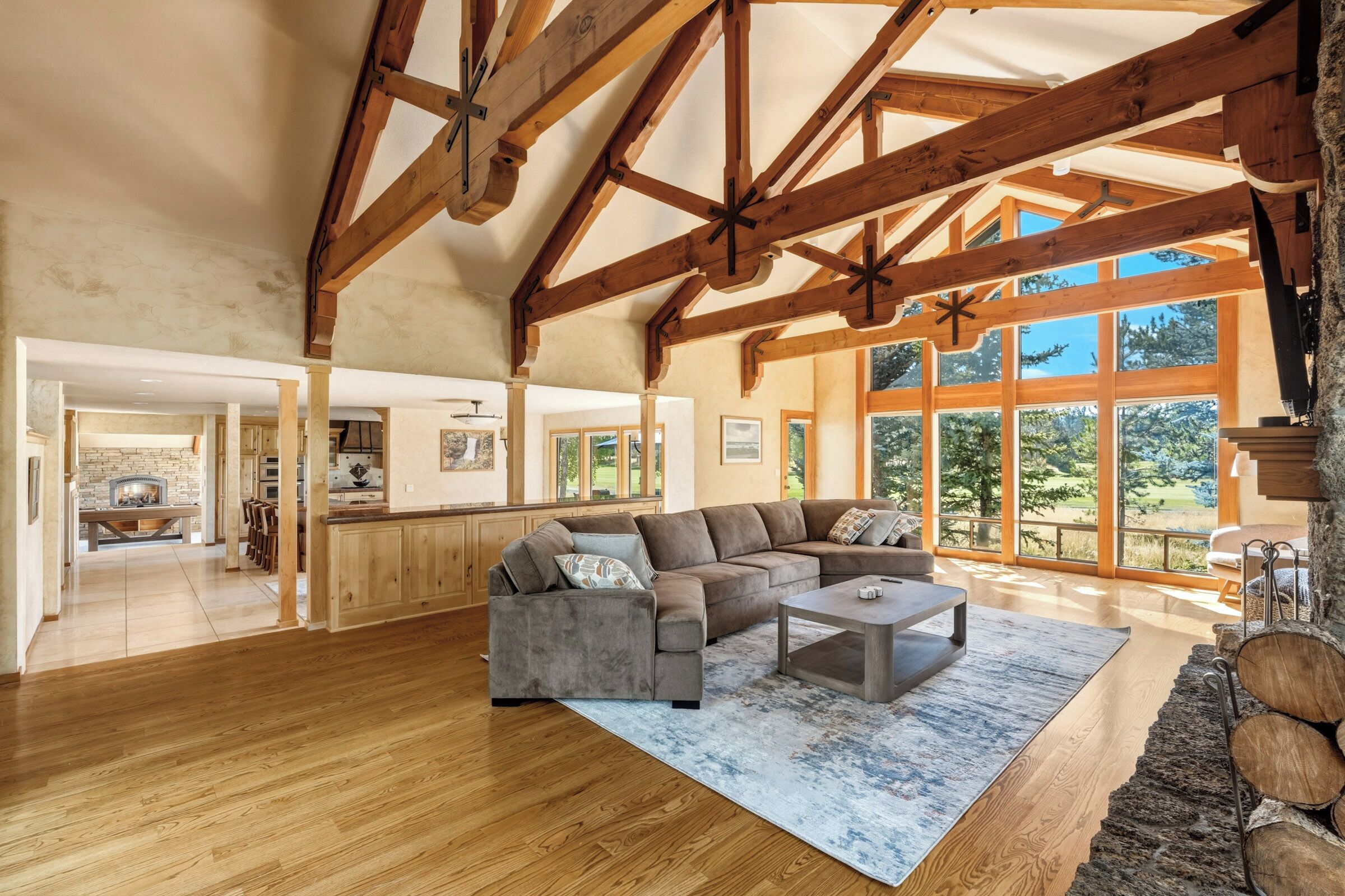A spacious living room with a wooden ceiling, a large window, and a stone fireplace.