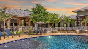 A pool area with lounge chairs, a covered seating area, and a stone wall. - Landing | Amazing 2BD, Courtyard, Pool (Cedar Park)