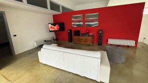 Ein Wohnzimmer mit weißem Sofa, Fernseher, roter Akzentwand und Heizkörper.