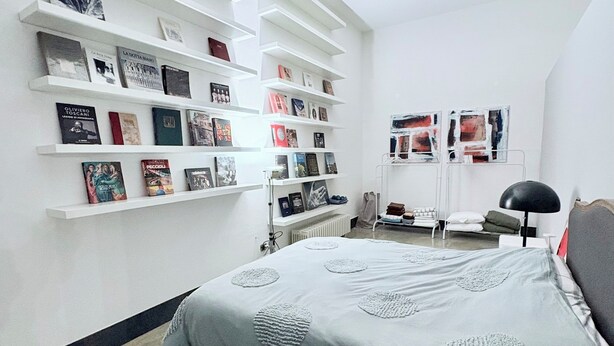 Ein Schlafzimmer mit einem Bett, weißen Regalen mit Büchern, einem Heizkörper und einem Schreibtisch.