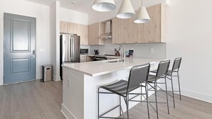 A modern kitchen with a central island, stainless steel appliances, and bar stools. - Landing | Incredible 2BD, Gym, Clubhouse (Mountain Brook)