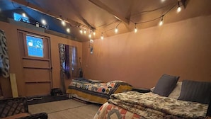 Une pièce confortable avec deux lits, une fenêtre, un ventilateur de plafond et des guirlandes lumineuses.