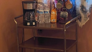 Un chariot en métal contenant une machine à café, des bouteilles d’eau, une tasse et un sac de collations.
