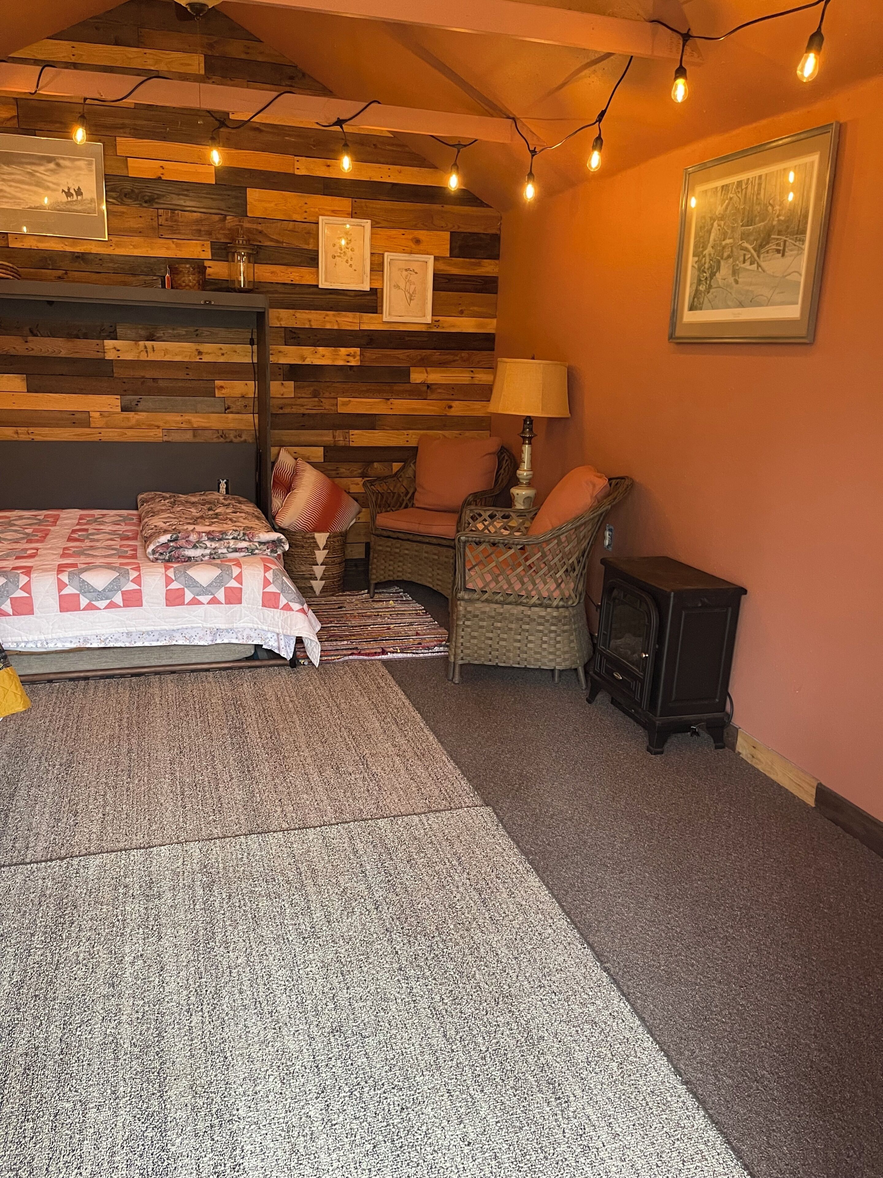 A cozy room with a bed, a chair, a small table, a lamp, and a wall with wooden panels and framed pictures.