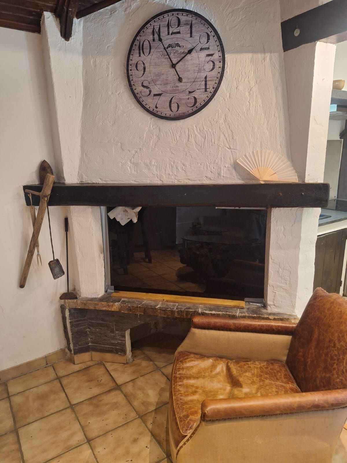 A room with a fireplace, a clock, and a leather chair.