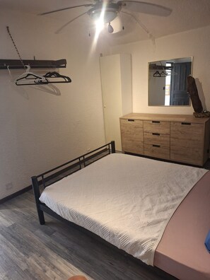 Un dormitorio con cama, cómoda de madera, espejo y ventilador de techo.