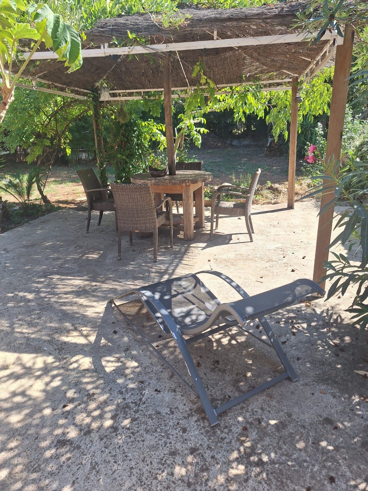 An outdoor seating area with a pergola, a round table, wicker chairs, and a metal chair.