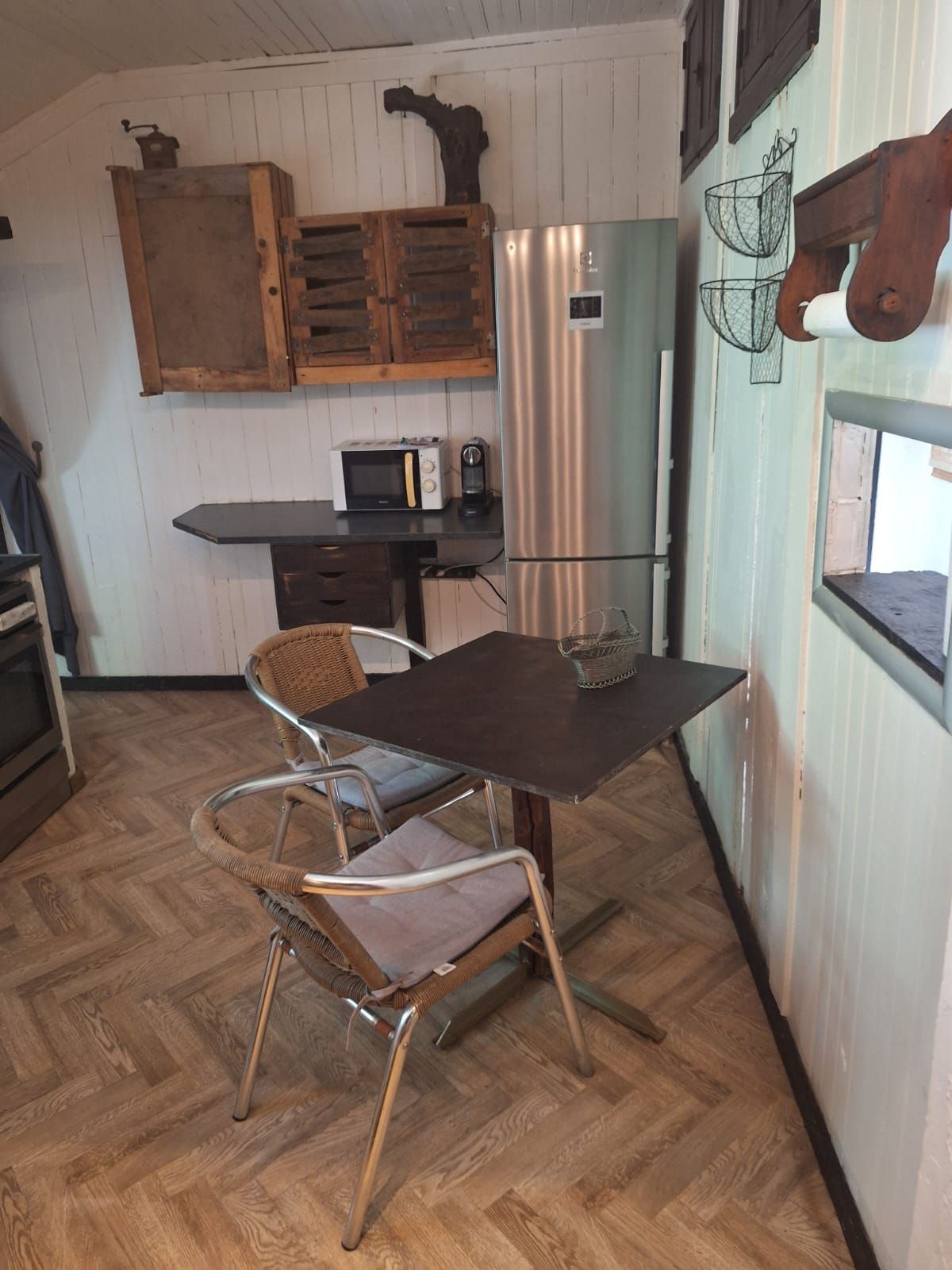 Une cuisine avec des meubles de rangement en bois, un réfrigérateur en acier inoxydable, un four à micro-ondes et une chaise en osier.