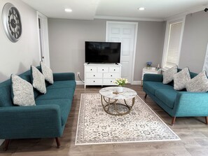 Un salon avec des canapés de couleur turquoise, un meuble de rangement blanc pour l’équipement audiovisuel, un téléviseur à écran plat et un tapis à motifs.