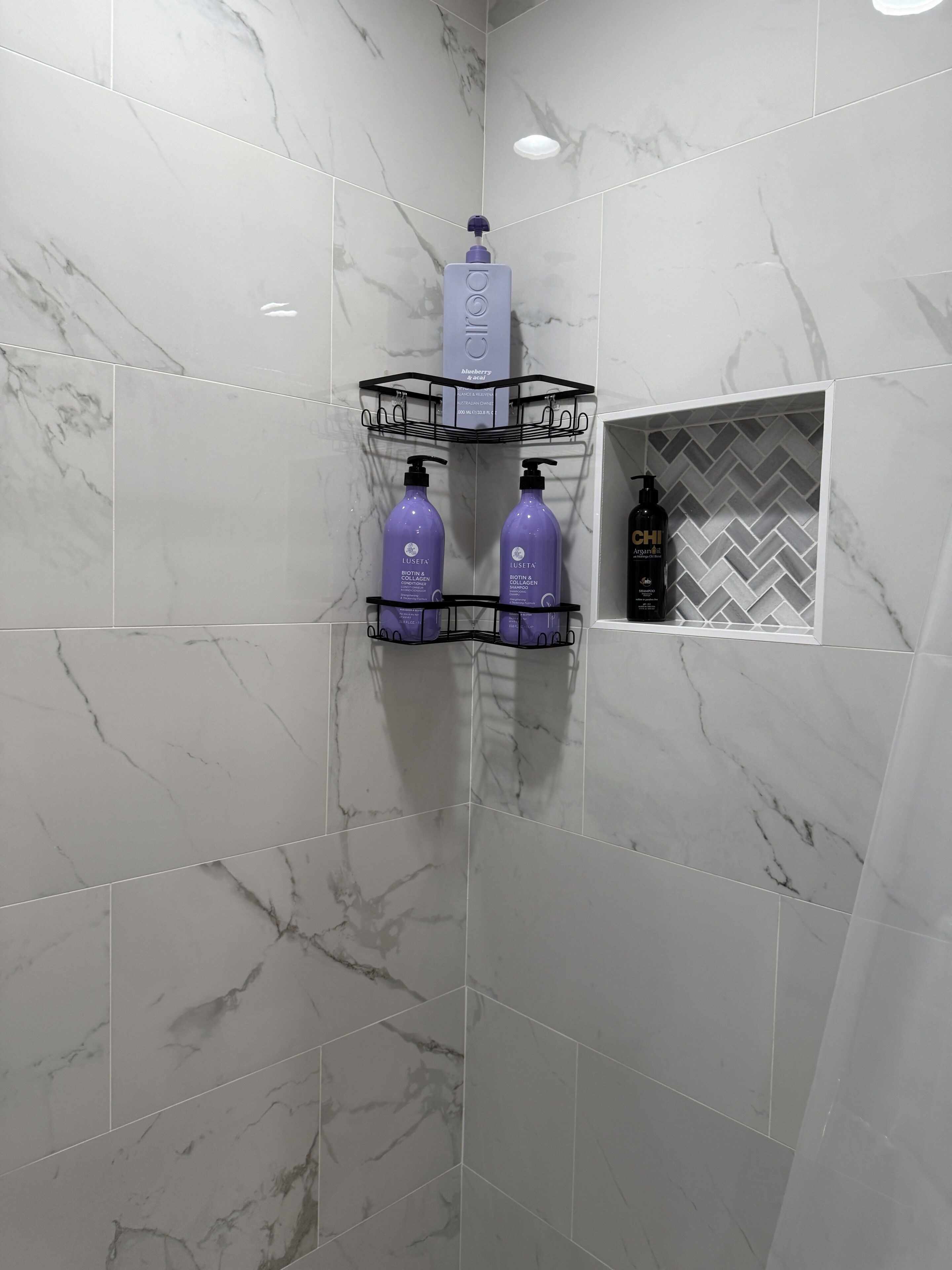 A bathroom with marble tiles, a shower area, and a shelf with toiletries.