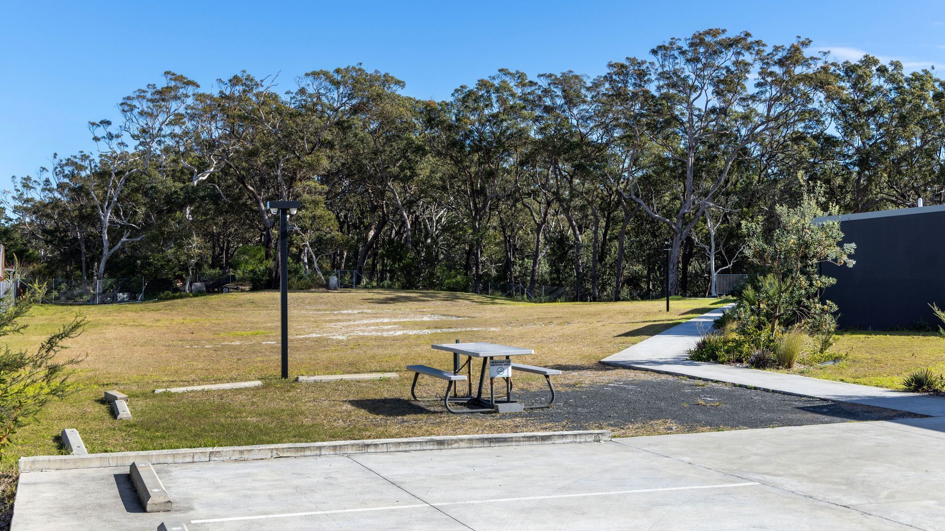 A parking area with a picnic table and benches, surrounded by trees and a building.