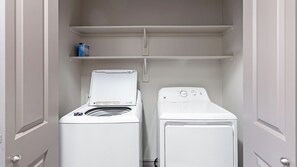 A laundry room with two white washing machines and a shelf above them. - Landing | Incredible 2BD, Clubhouse, Pool (Fort Worth)