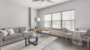 A modern living room with a grey sofa, a round coffee table, a side table, a floor lamp, and a dining area with a white table and chairs. - Landing | Incredible 2BD, Clubhouse, Pool (Fort Worth)