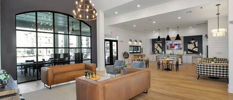 A spacious living area with a large window, a modern chandelier, and a mix of seating options including sofas and chairs.