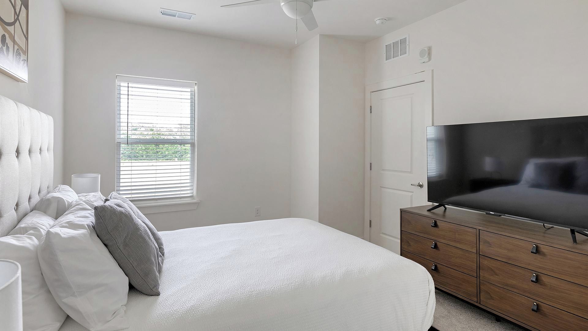 A bedroom with a bed, a dresser, a television, and a window.
