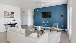 Ein modernes Wohnzimmer mit einer Couch, einem Couchtisch und einem an einer blauen Wand befestigten Fernseher.