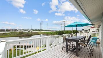 A wooden deck with a table and chairs, overlooking a body of water and buildings in the distance.