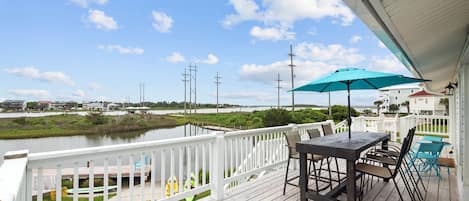 A wooden deck with a table and chairs, overlooking a body of water and buildings in the distance.