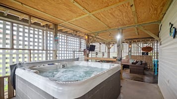 A hot tub in a wooden cabin with a lattice window, a couch, and a sign indicating a 'Hot Tub' service.