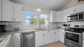 A modern kitchen with white cabinets, stainless steel appliances, a dishwasher, and a window with a view of palm trees.